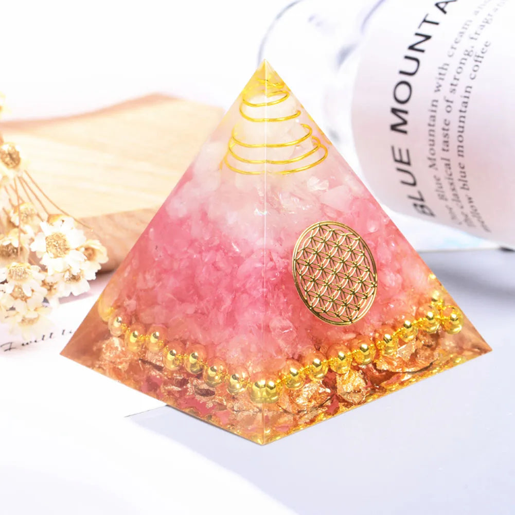 Pyramid-shaped pink and gold decorative item on a white surface with a blurred product in the background.