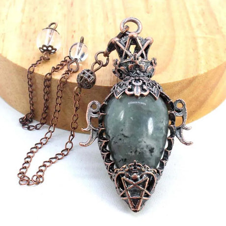 Decorative pendant with green stone and intricate metalwork on a wooden background