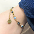 Gold bracelet with eye-shaped charms on a wrist, wearing a blue garment.
