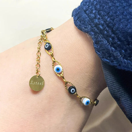 Gold bracelet with eye-shaped charms on a wrist, wearing a blue garment.