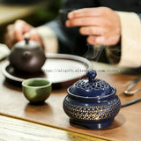 Ceramic incense burner with intricate design on a wooden table, with a teapot and cup in the background.