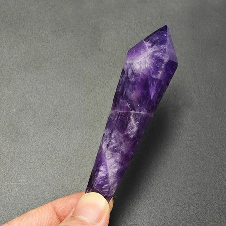 Purple crystal held by a hand against a gray background
