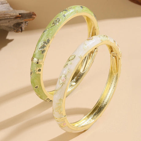 Two gold bangles with green and white patterns on a beige background