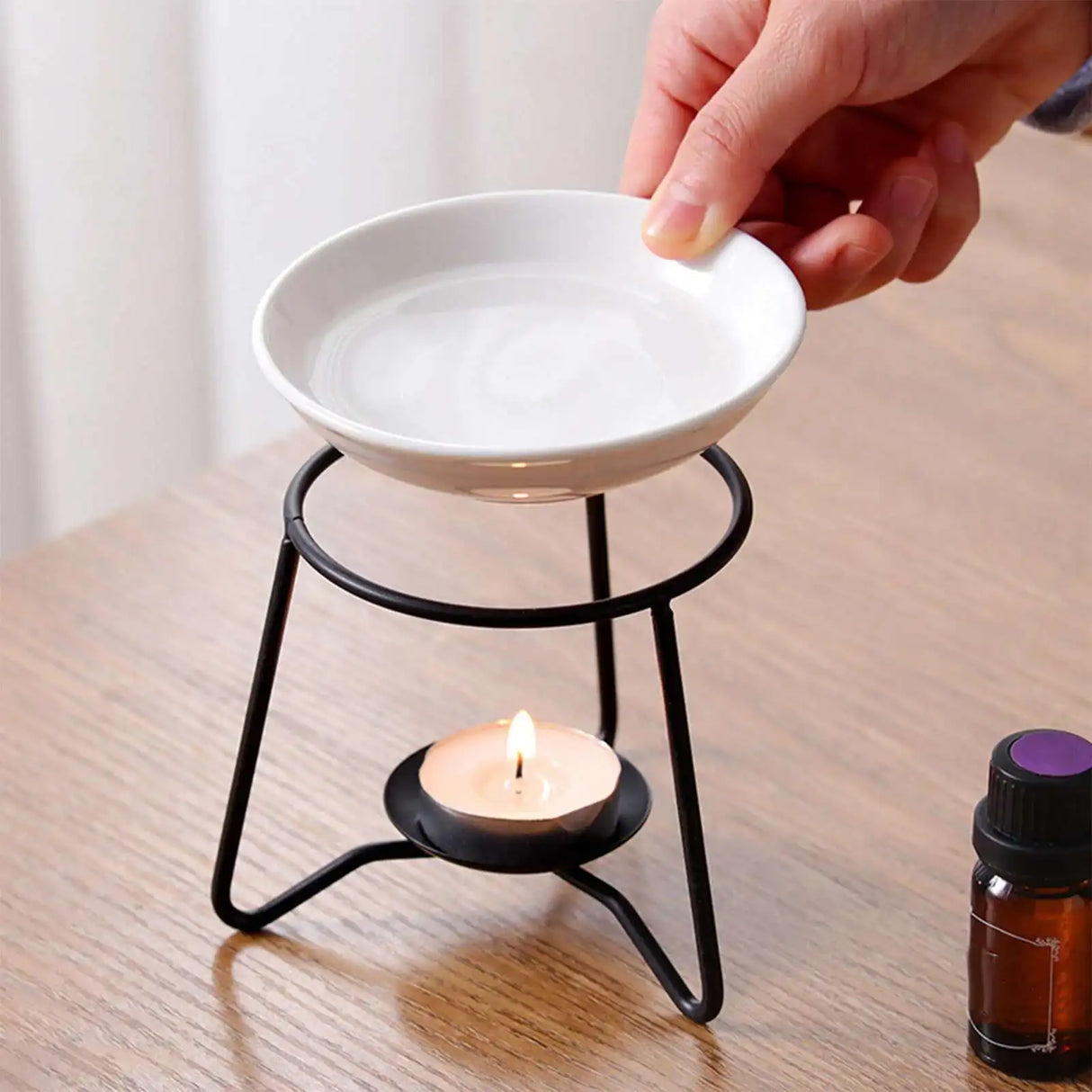Person pouring water into a white ceramic bowl on a black essential oil diffuser with a lit candle.