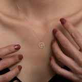 Gold necklace with a tree-of-life pendant on a person's neck, with hands gently touching the skin.