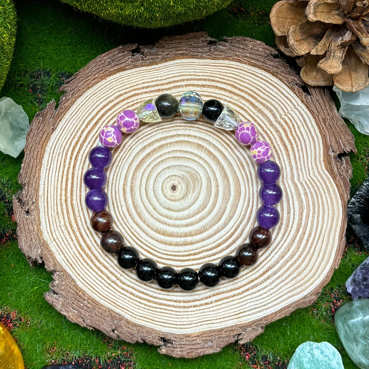 Beaded bracelet with purple and black beads on a wooden stump with greenery