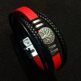Bracelet with red and black leather straps and a silver tree-of-life emblem on a dark background