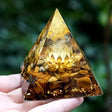 Pyramid-shaped crystal with a lotus design held by a hand against a blurred green background
