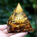 Pyramid-shaped crystal with a lotus design held by a hand against a blurred green background