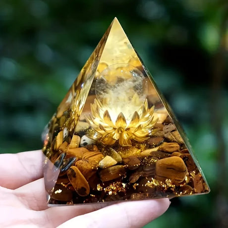 Pyramid-shaped crystal with a lotus design held by a hand against a blurred green background