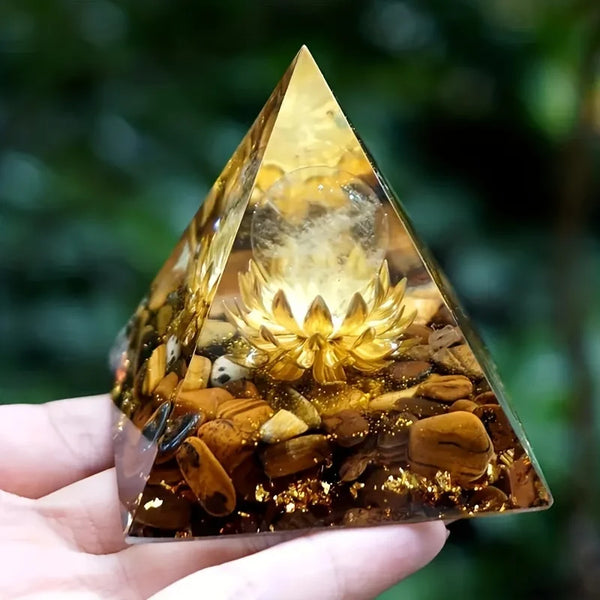 Pyramid-shaped crystal with a lotus design held by a hand against a blurred green background