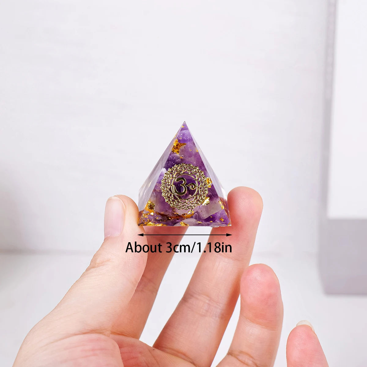 Triangular crystal with 'Om' symbol held between fingers against a white background