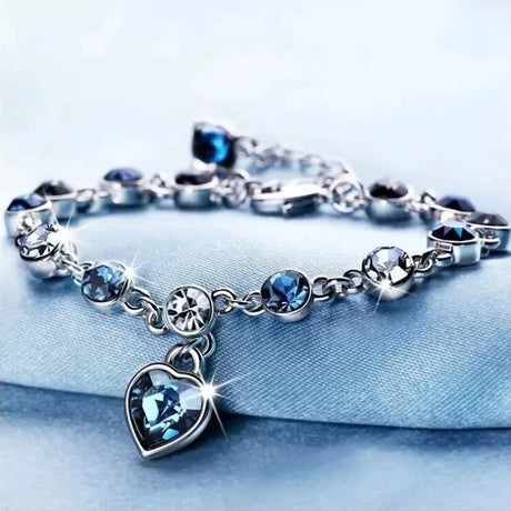 Silver bracelet with blue heart charm on a light blue background