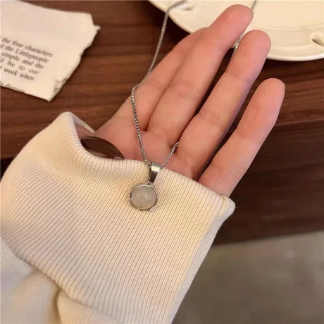 Hand wearing a silver necklace with a round pendant on a wooden surface.