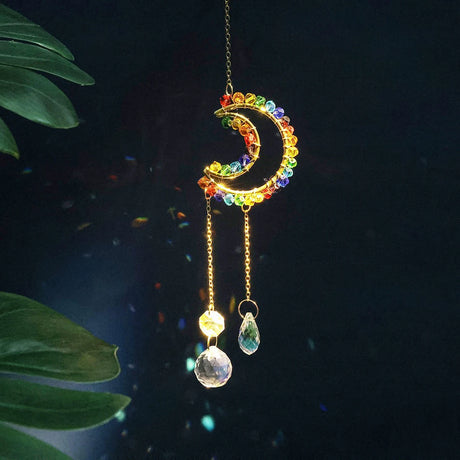 Colorful moon-shaped hanging ornament with crystals on a dark background