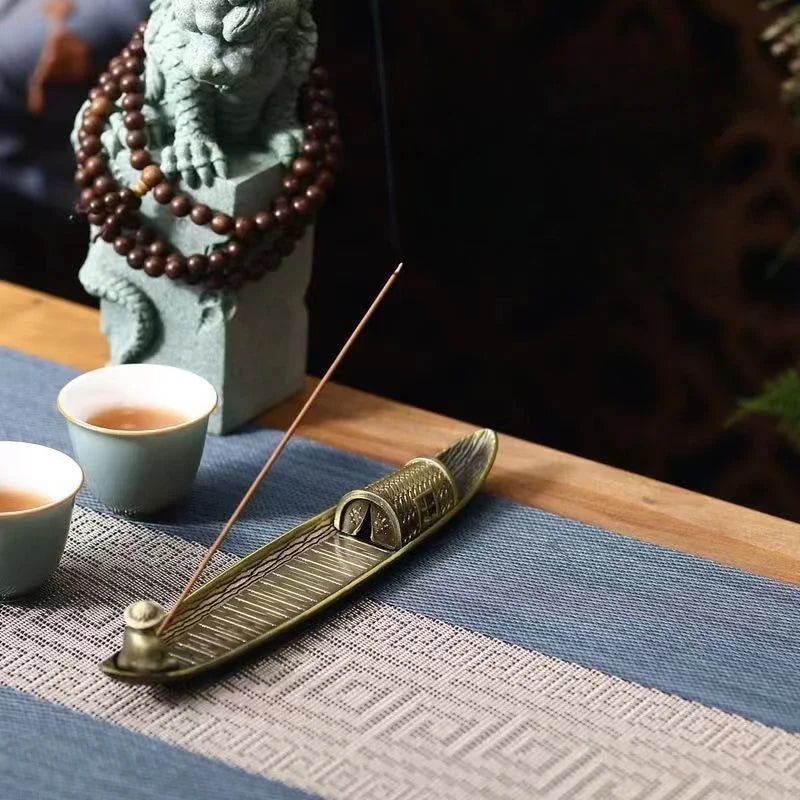 Incense burner with incense stick on a table with cups and a decorative statue in the background