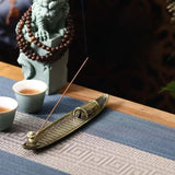 Incense burner with incense stick on a table with cups and a decorative statue in the background