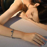Woman lying down wearing a bracelet with blue beads on a neutral background