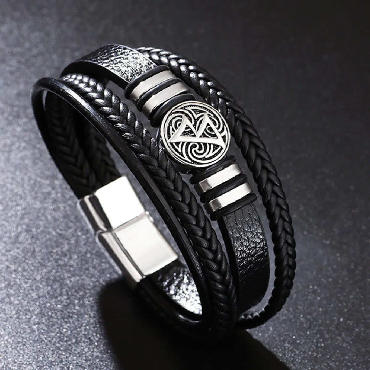 Black braided leather bracelet with silver metal accents on a dark background