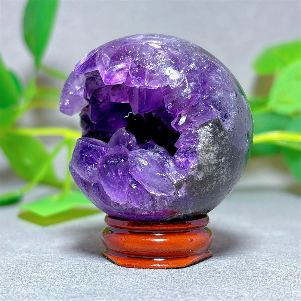 Amethyst crystal sphere on a stand with a blurred green plant background