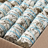 White sage smudge sticks tied with blue string in a cardboard box