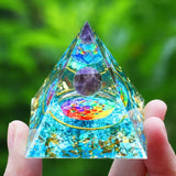 Crystal pyramid with colorful interior held by a hand against a green blurred background