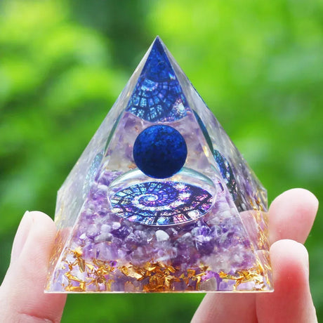 Pyramid-shaped crystal with purple and blue colors held by a hand against a green blurred background