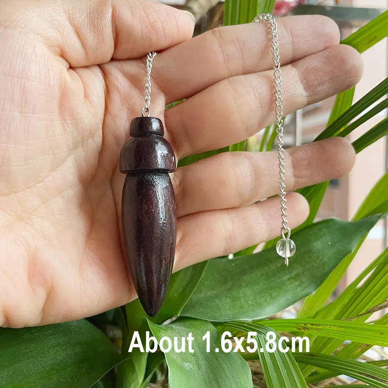 Hand holding a wooden pendant with a chain against a leafy background