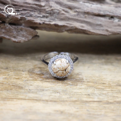 Silver ring with a beige stone on a wooden surface