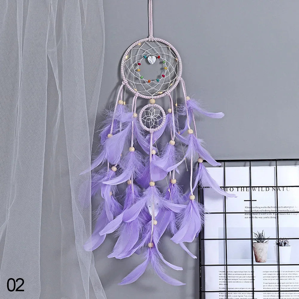 Purple dreamcatcher with feathers hanging against a gray curtain.