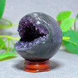 Geode crystal with purple interior on a stand against a blurred green plant background