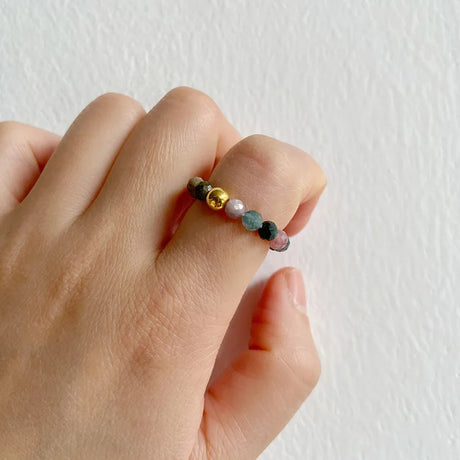 Hand wearing a ring with multicolored beads on a plain background