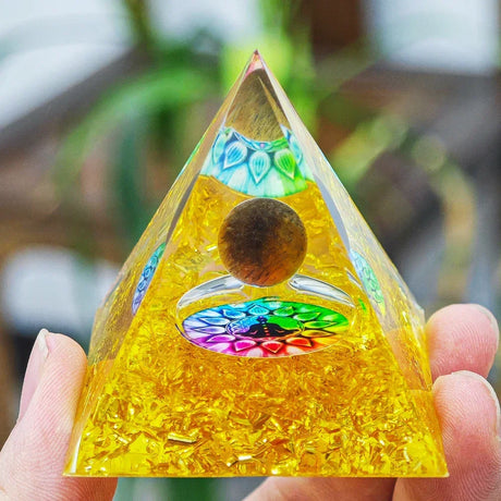 Triangular pyramid with colorful interior held by a hand against a blurred natural background
