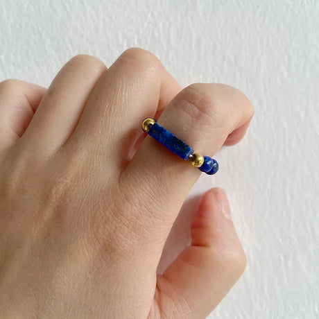 Hand wearing a blue beaded ring with gold accents on a white background