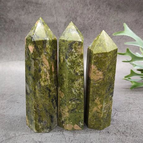 Three green crystal points on a gray surface with a plant in the background