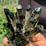 Hand holding a cluster of crystal formations with a blurred natural background