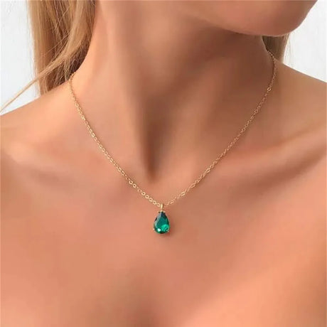 Gold necklace with a green teardrop pendant on a model