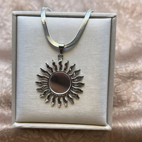 Silver sun-shaped pendant necklace on a white box with a beige background