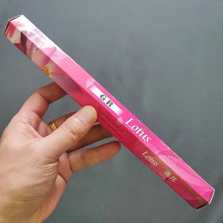 Hand holding a pink cosmetic product with 'Lotus' branding against a gray background