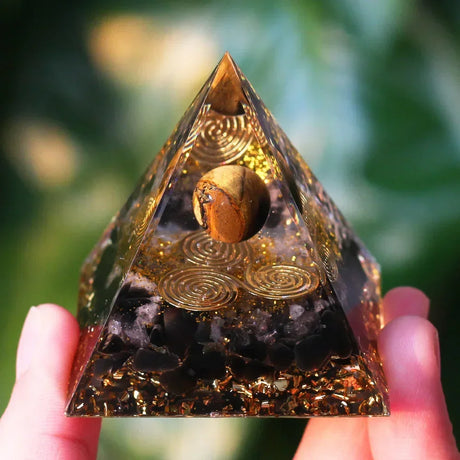 Pyramid-shaped crystal with gold spiral patterns held by a hand against a blurred green background