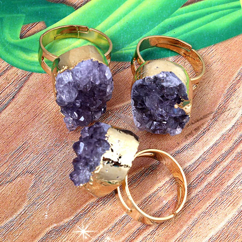 Three gold rings with purple crystal-like stones on a wooden surface