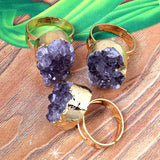 Three gold rings with purple crystal-like stones on a wooden surface