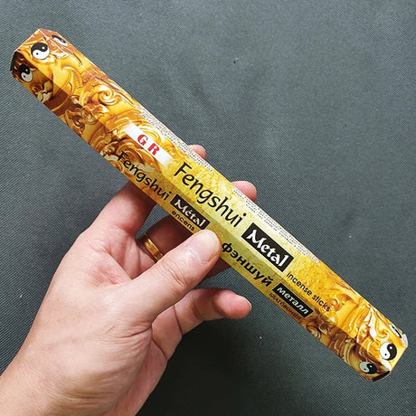 Hand holding a package of Fengshui Metal incense sticks against a dark background