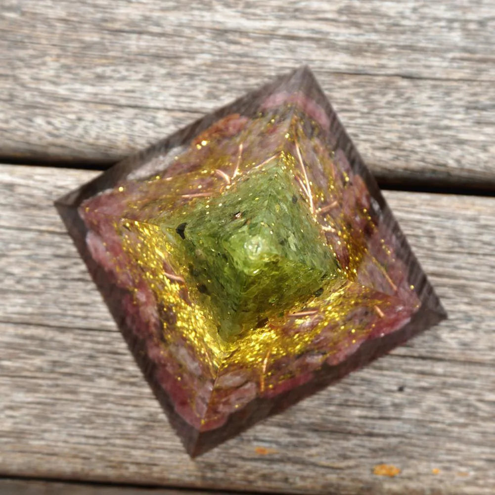Crystal pyramid with a green stone on a wooden surface