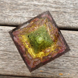 Crystal pyramid with a green stone on a wooden surface