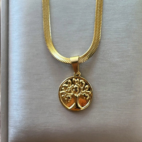 Gold necklace with a tree-of-life pendant on a metallic surface