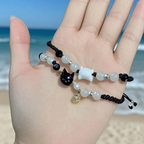 Hand wearing a bracelet with cat charm against a beach background