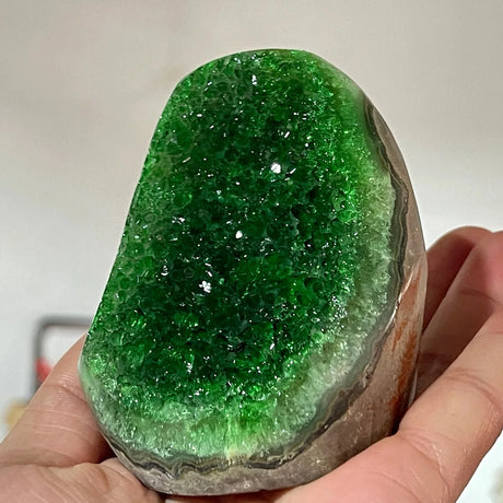 Green crystal rock held in a hand against a neutral background
