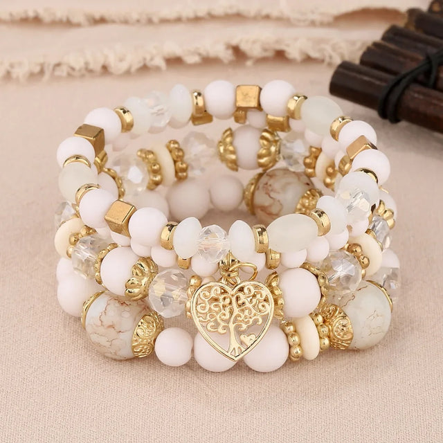 Stack of white and gold beaded bracelets with a heart charm on a beige fabric background