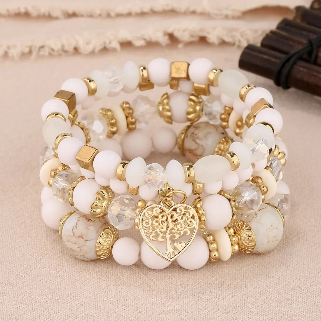 Stack of white and gold beaded bracelets with a heart charm on a beige fabric background